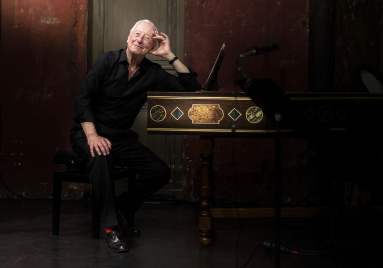 William Christie sitting at a harpsichord smiling