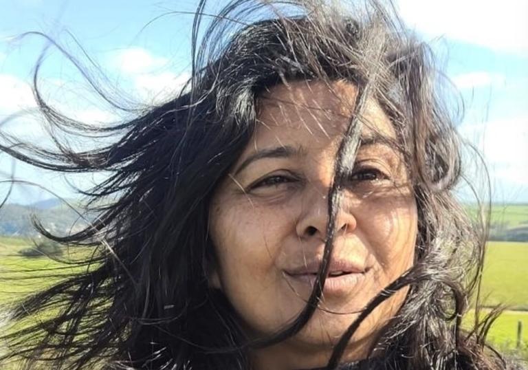Davel Holvek Patel standing in a field, her hair is being blown by the wind