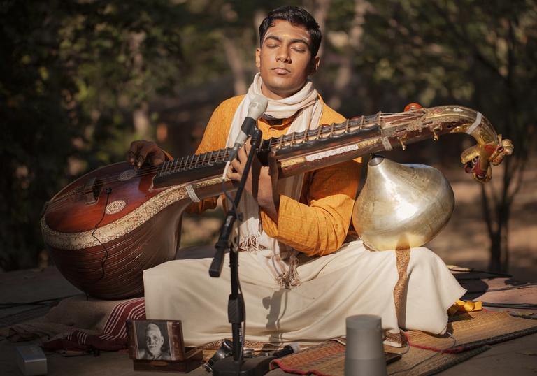 Ramana Balachandran sitting in a garden playing his veena - a large stringed instrument