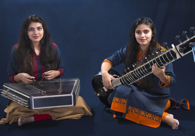 Sanskrati and Prakrati Wahane playing their instruments in front of a dark background