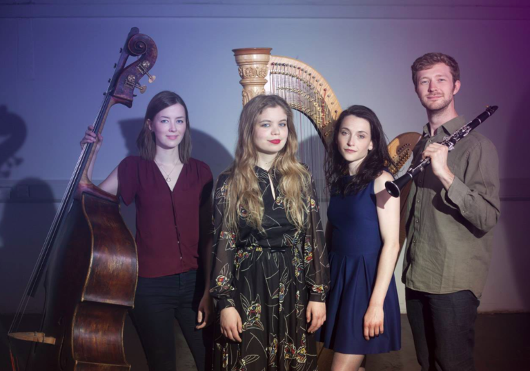 The Hermes Experiment standing with their instruments: a double bass, a clarinet and a harp