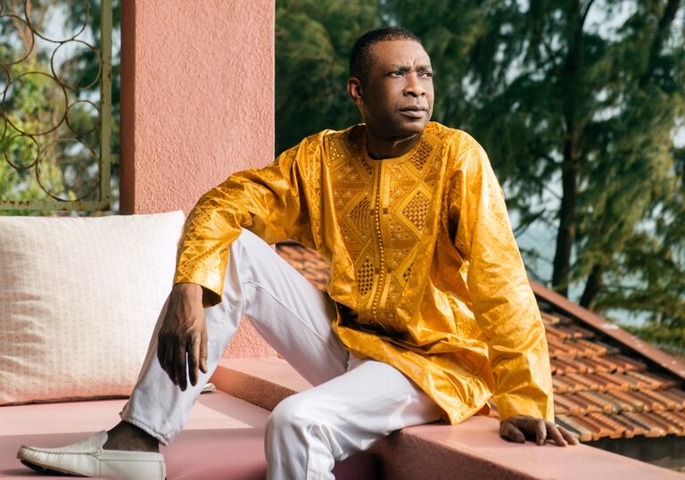 Youssou N'Dour sitting on a roof terrace, looking over his left shoulder