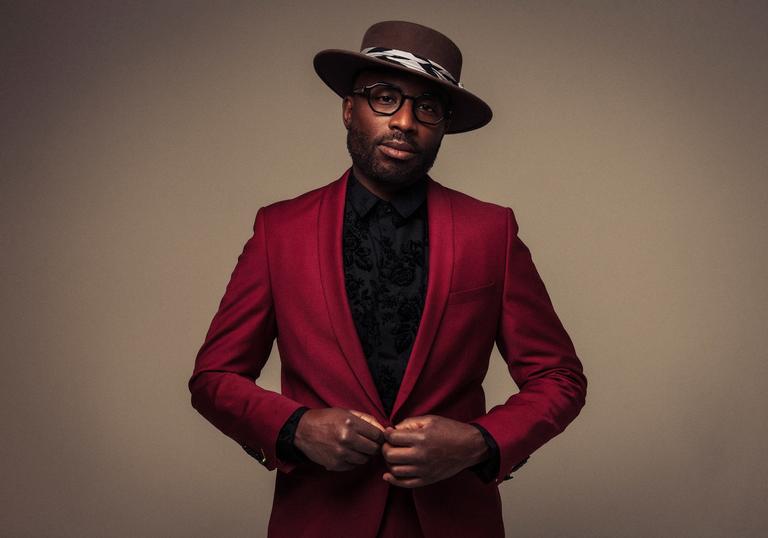 Alexis Ffrench wearing a burgundy suit and wide-rimmed hat