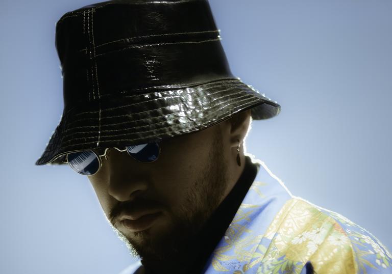 close up photo of Sofiane Pamart against a pale blue backdrop, wearing bucket hat and sunglasses