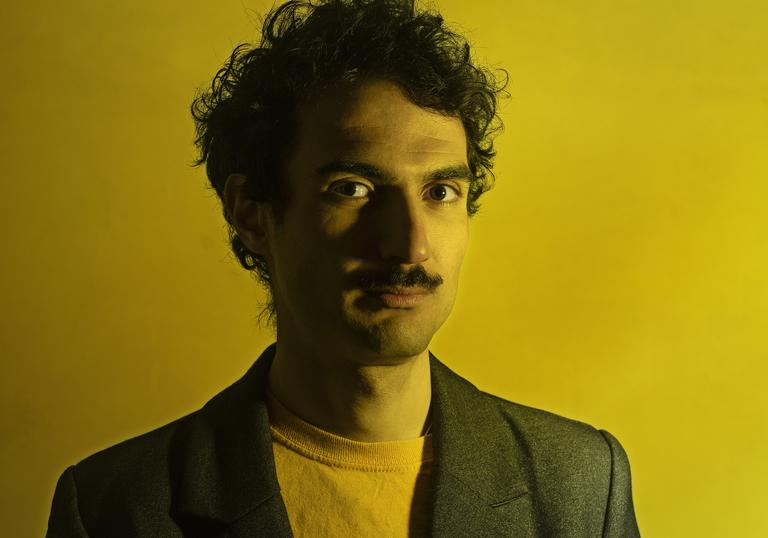 Tigran Hamasyan wearing a yellow t shirt and black blazer