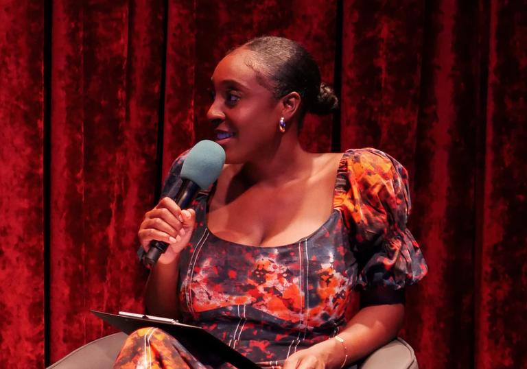 Black female in sitting in a chair holding a microphone