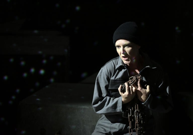 Sinead Campbell-Wallace performs as Leonore, wearing a prison jumpsuit and holding shackles