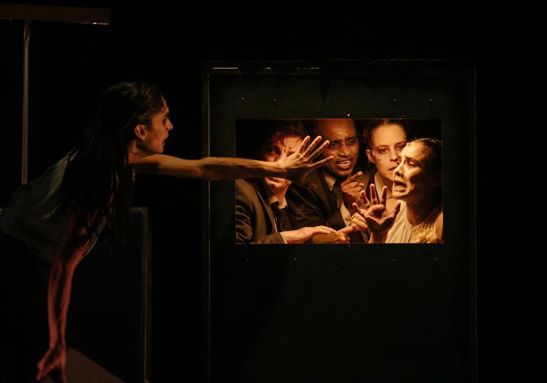 Actors on stage: four people are trapped behind a door, looking desperately at another person reaching towards them.