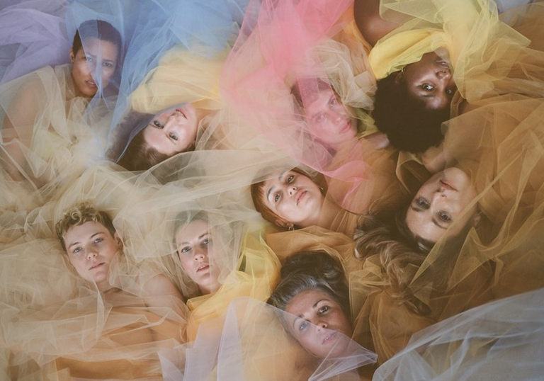 9 people lying in amongst different coloured fabric 