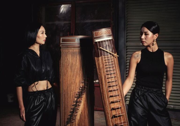 Dal:um standing dressed in black with a black backdrop, holding their instruments