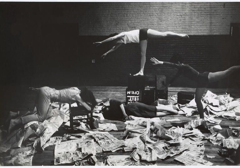 Image shows 4 dancers posing horizontally amongst newspapers 