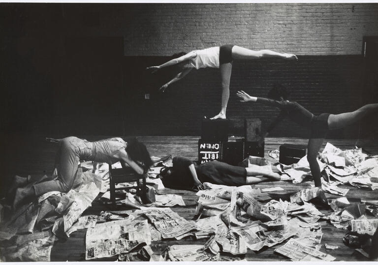 Image shows 4 dancers posing horizontally amongst newspapers