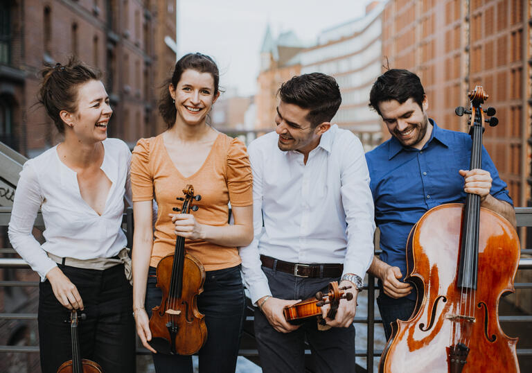The Aris Quartett standing on a bridge holding their instruments