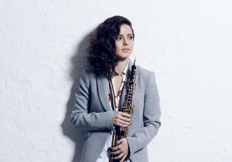 Cristina Gomez Godoy standing in front of a white wall holding her oboe