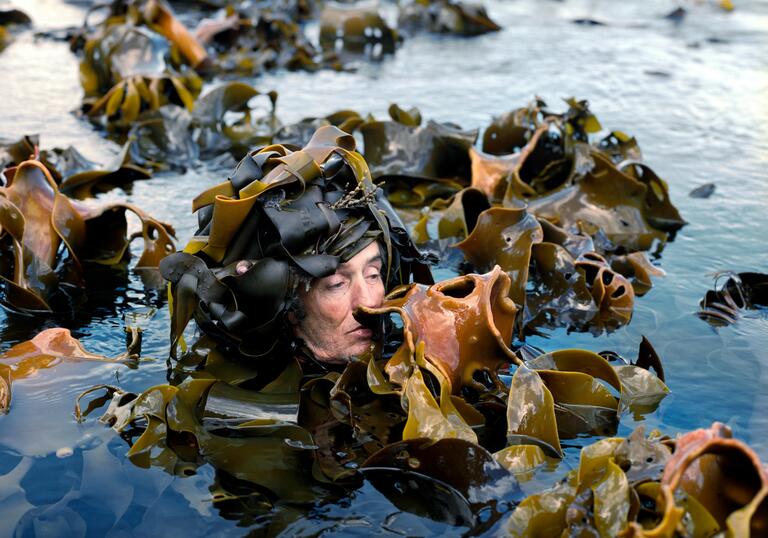 Man in seaweed immersed in water up to neck