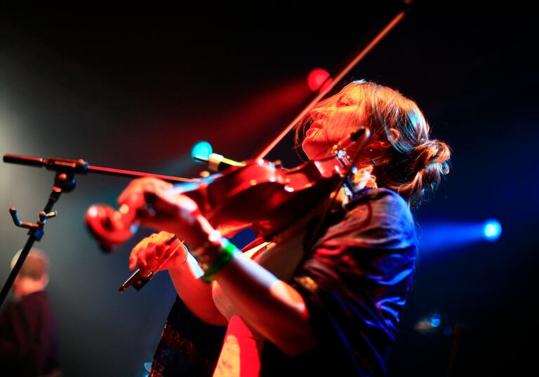 Eliza Carthy playing the fiddle under dynamic lighting on stage