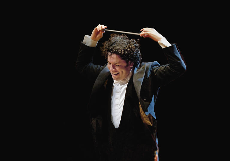 Gustavo Dudamel smiling while holding his baton above his head