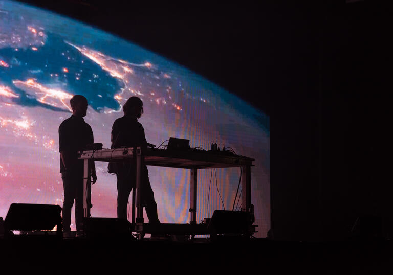 Dynamic shot of The End of The World playing on stage amidst the backdrop of planet earth