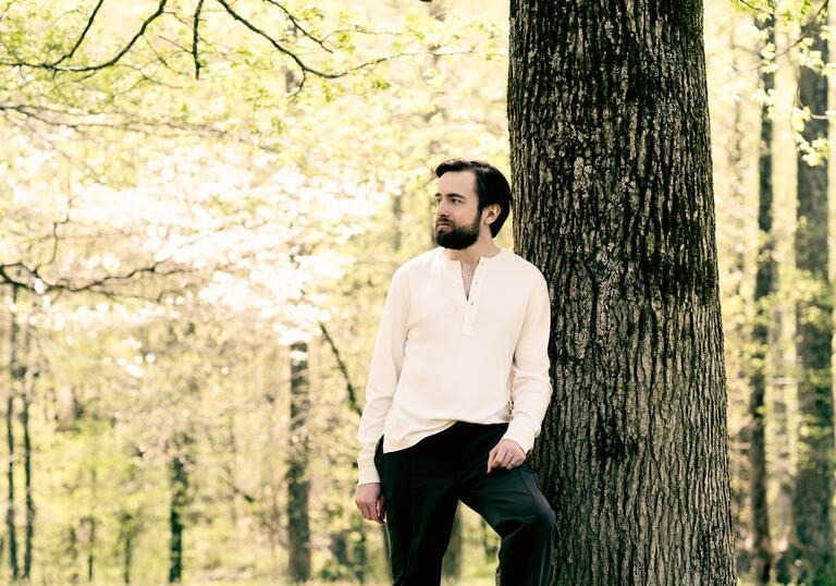 Daniil Trifonov standing next to a tree trunk