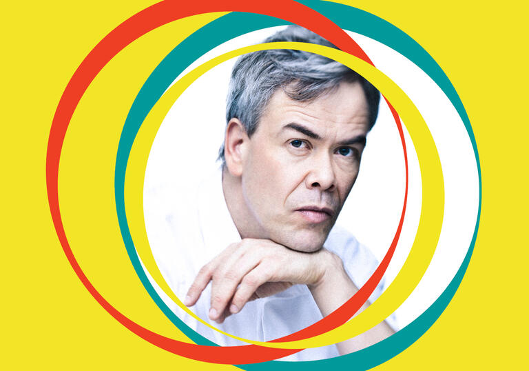 Hannu Lintu leans on his hand. Yellow BBC SO branding surrounds his centralised image