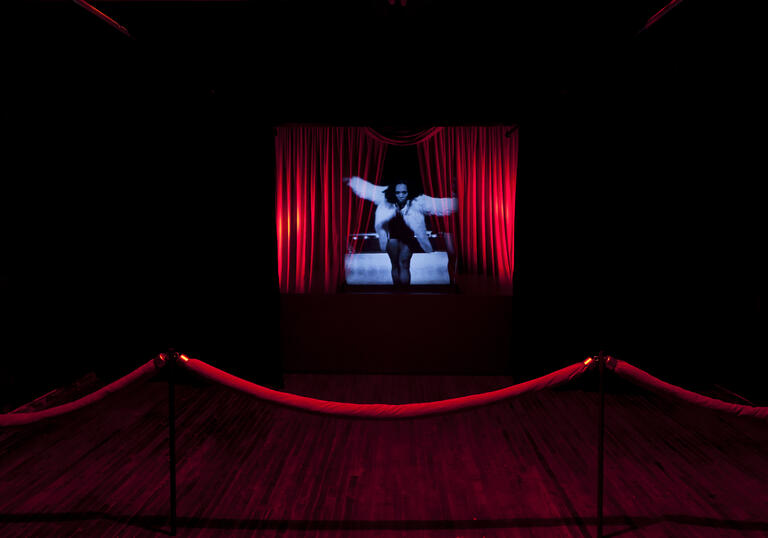 Woman in blue light on the middle of a stage with red curtains on either side