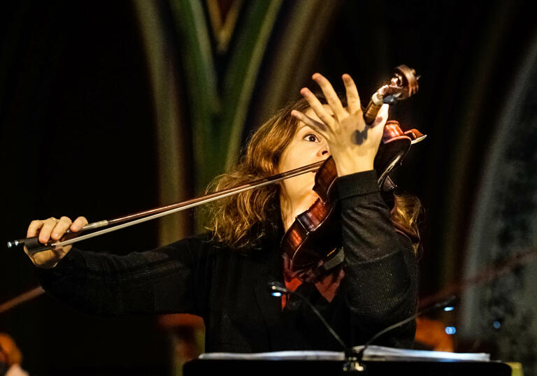 Patricia Kopatchinskaja plays her violin - it's held in front of the right hand side of her face 