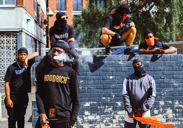 The ensemble, wearing Hoodrich clothing stand on and around a wall.