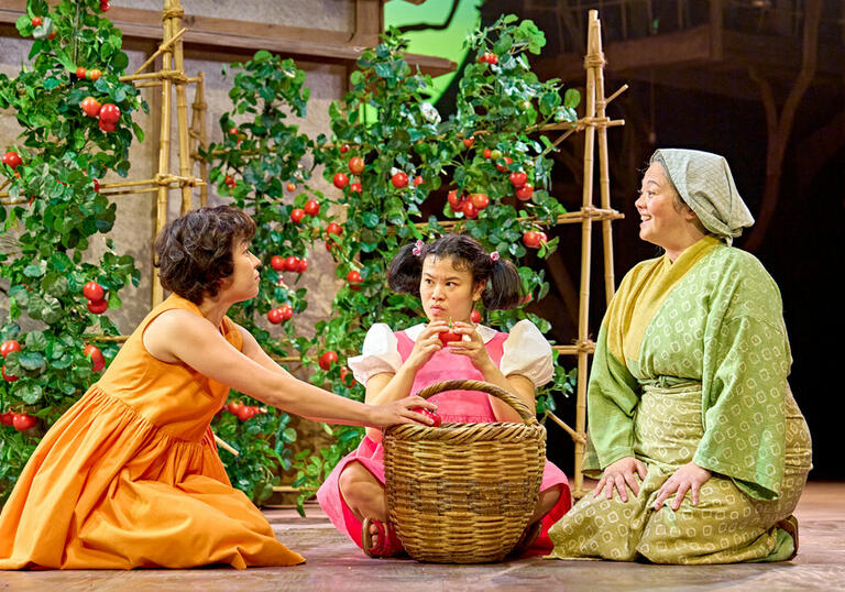 Satsuki (Ami Okumura Jones), Mei (Mei Mac) and Granny (Jacqueline Tate) sitting on the floor around a large wicker basket 