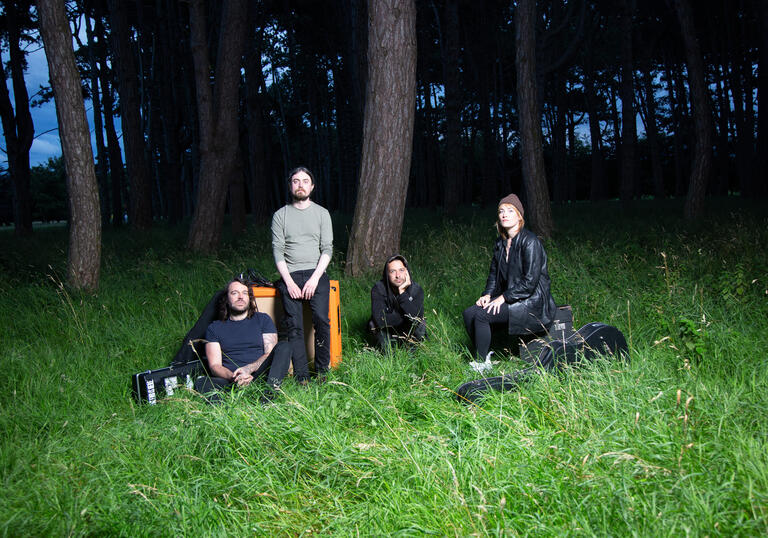 Group shot of Lankum sitting on a patch of moonlight grass next to a forest 