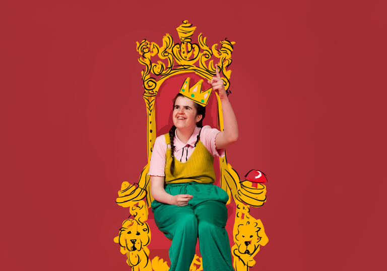 A photo of Rachel sitting on an illustrated golden throne wearing an illustrated golden crown. She is wearing green trousers and a pink top with a yellow top on top of it. She is smiling with her finger pointed towards the sky.