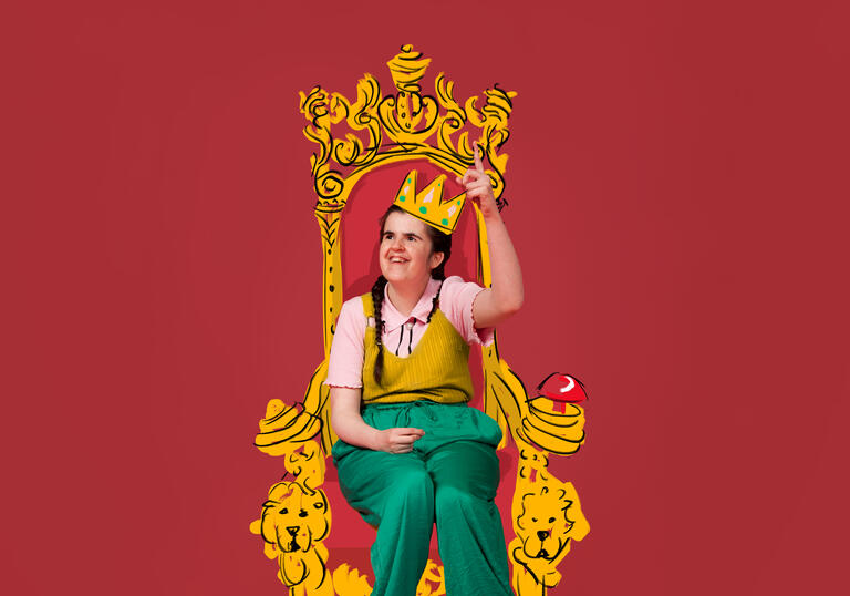 A photo of Rachel sitting on an illustrated golden throne wearing an illustrated golden crown. She is wearing green trousers and a pink top with a yellow top on top of it.  She is smiling with her finger pointed towards the sky.