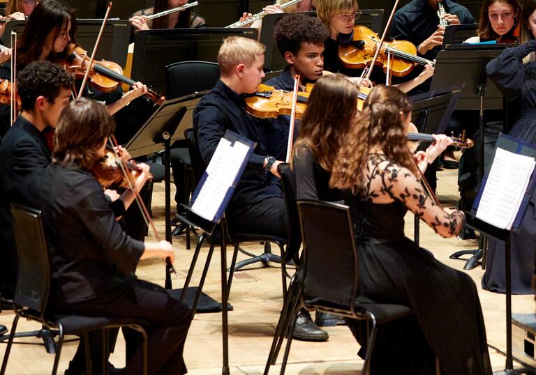 The string and woodwind sections of the London Schools Symphony Orchestra performing on stage