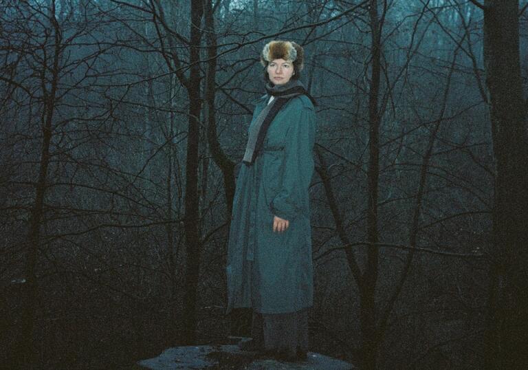 Wintry, analogue shot of Christina standing on a tree stub in a melancholic woodland