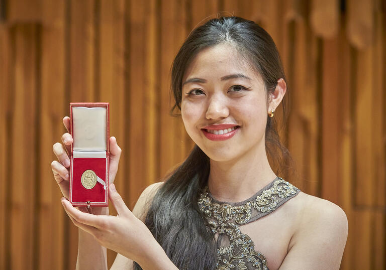 Gold Medal 2022 winner Stephanie Tang holding up the medal and smiling