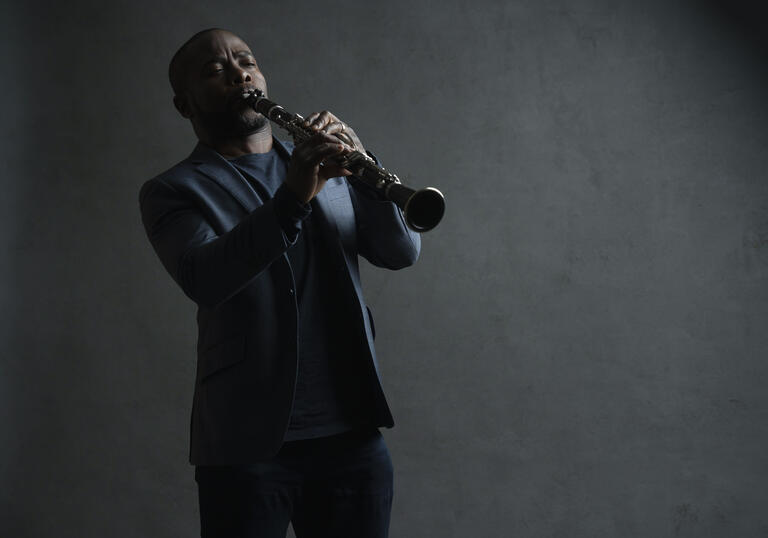 Anthony McGill playing his clarinet in front of a grey background