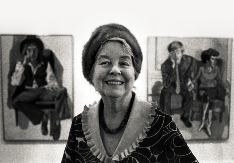 A black and white photograph of Alice Neel smiling to camera.