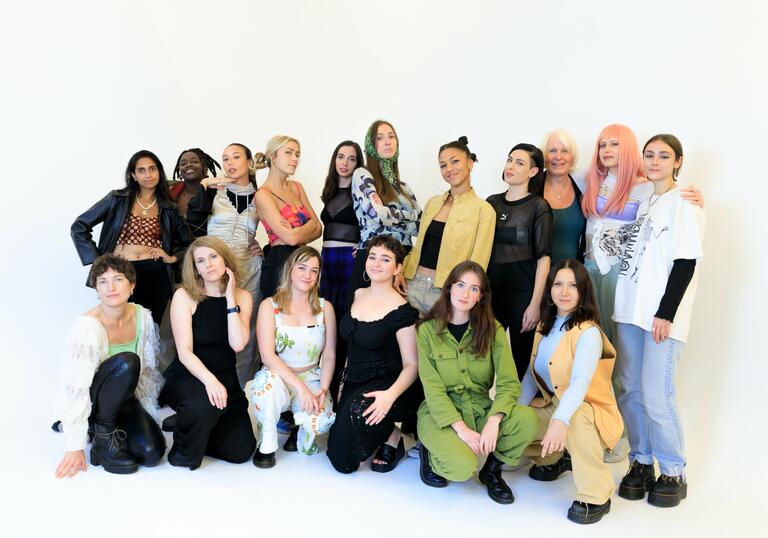 The Sisu DJ collective crew, 17 people stood together in a white room.