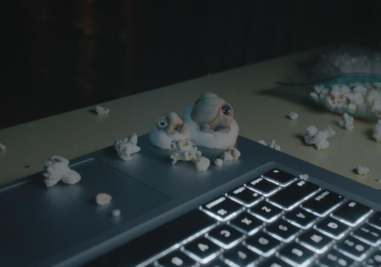 Marcel, a small antrhopomorphic shell, and his grandma sit on a laptop surrounded by popcorn. 