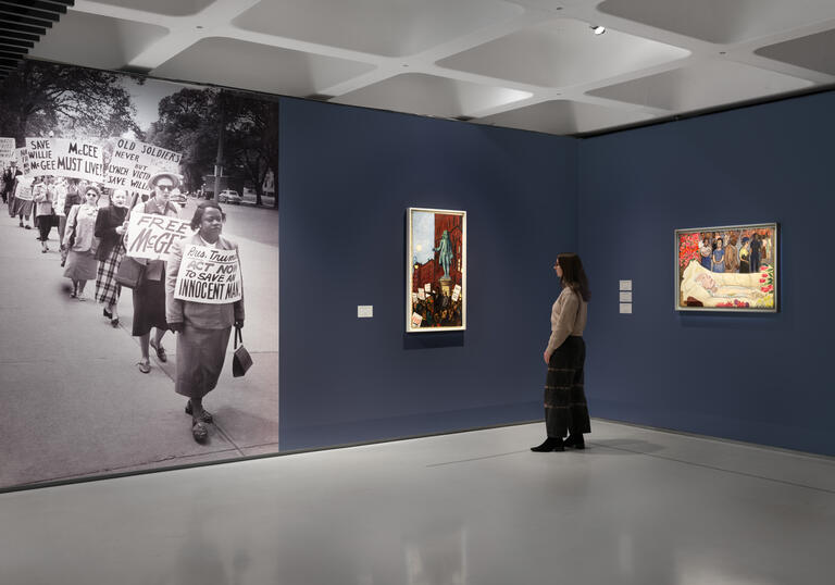 Woman standing in front of two portrait paintings by Alice Neel.