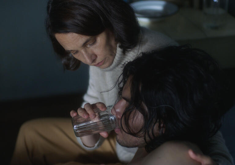 A woman feeds a young man water in a still from 1976
