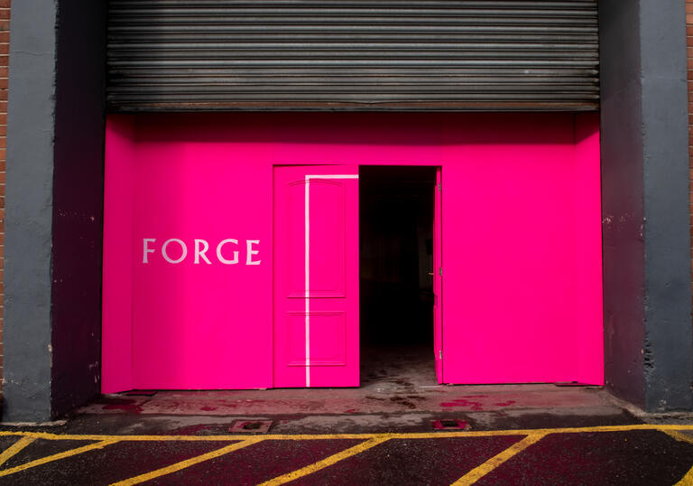 A pink entrance with a single open door. The word 'Forge' is written on the pink wall in white writing.