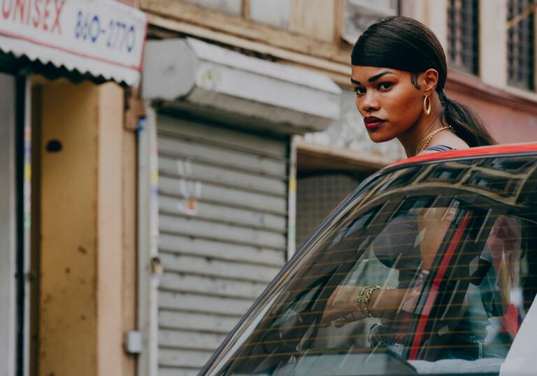 A woman looks out over a car on an urban street in a still from A Thousand and One.