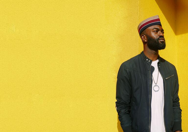 Inua Ellams standing against a bright yellow background