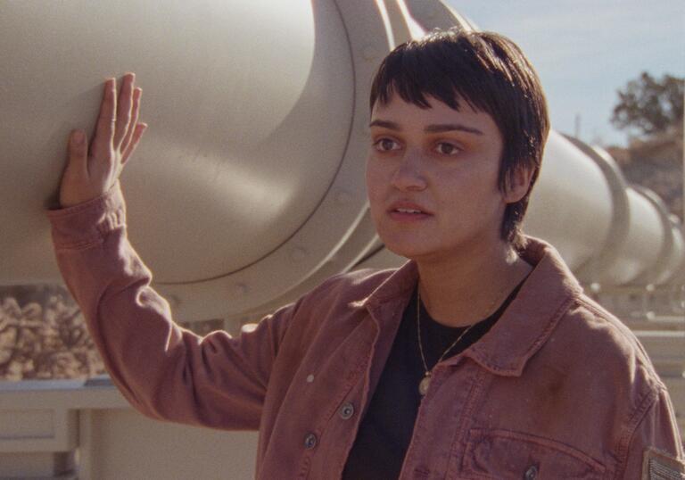 A  woman touches the side of a pipeline with a serious look on her face in a still from How To Blow Up A Pipeline