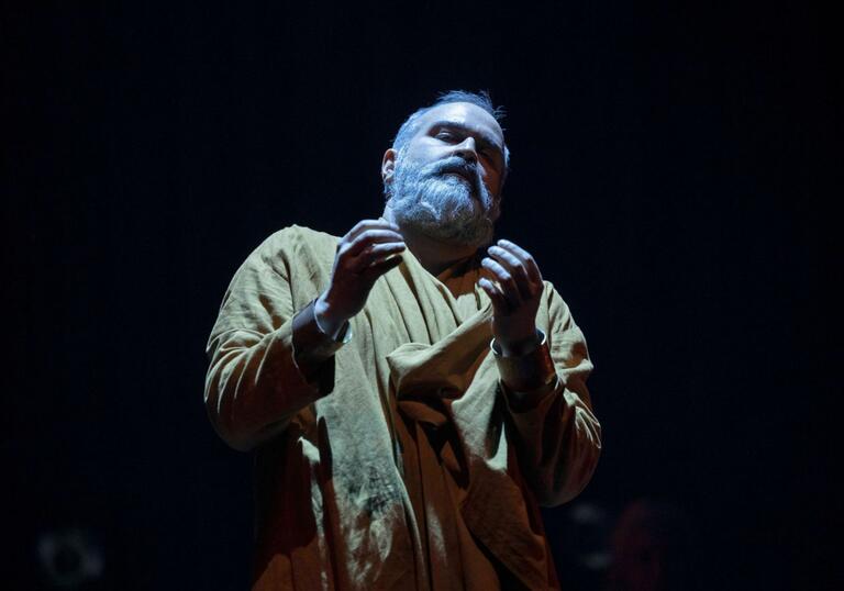 A performer holds out their hands in front of them. The room is dark.