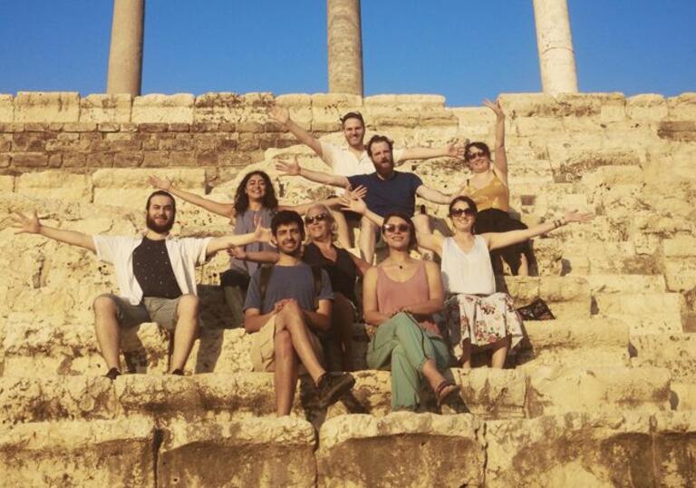 Group of people sat on some ancient steps with their arms wide, looking at the camera.