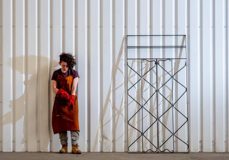 Performance artist Rachel Mars stands against a white backdrop next to a gate