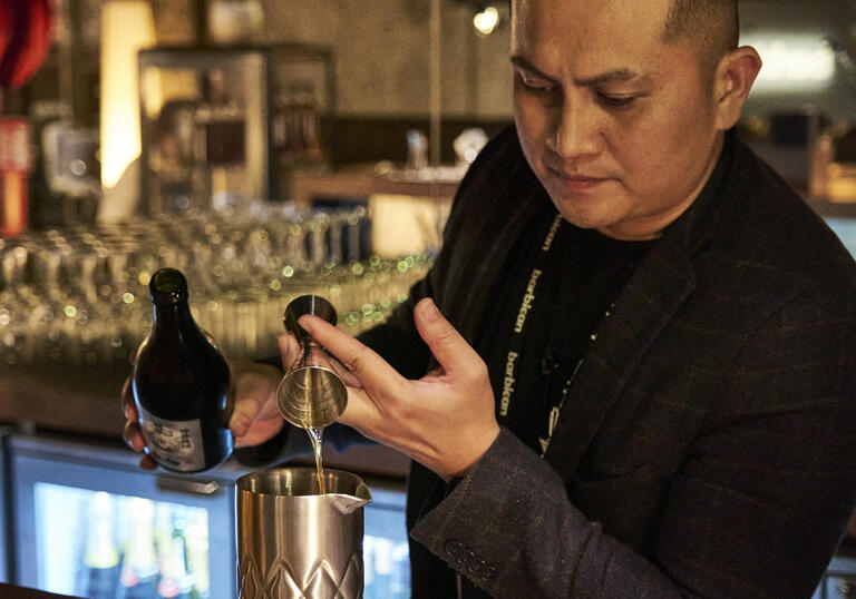 Man pouring a shot of prosecco into a steel jug at a wooden bar.