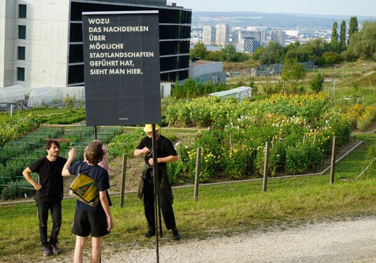 photo of three people standing outside a building holding a sign written in German