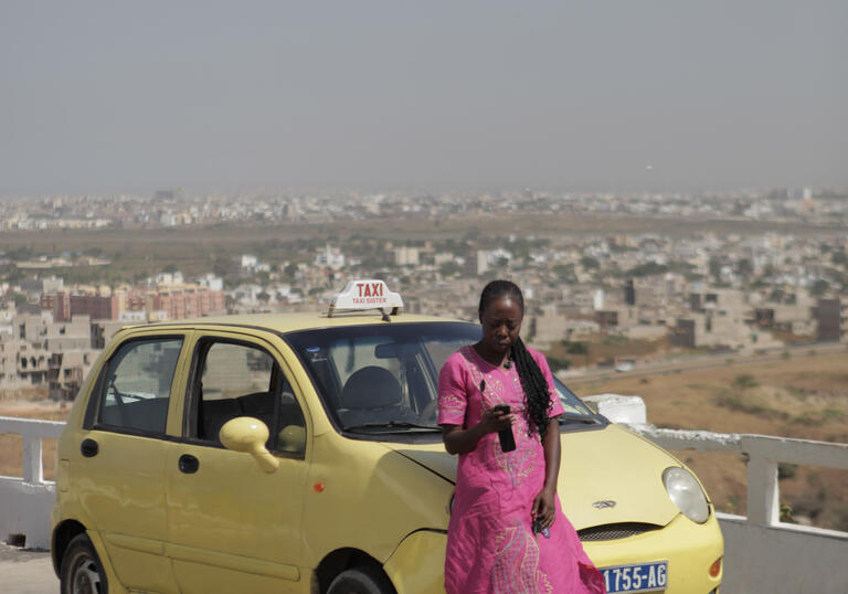 A woman in a pink dress stands in front of a yellow car